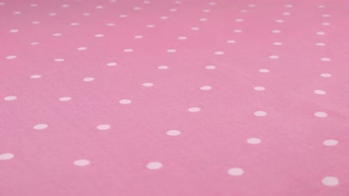 Close-up view of the mauve pink with white polka dots cotton fabric rotated on the display case.
