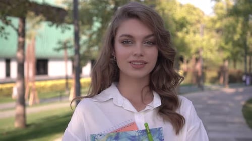 Attractive Woman Smiling with Notebooks in Green Park
