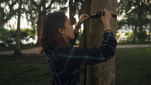 Voici une photo d'une jeune femme asiatique enroulant un hamac autour d'un arbre dans un parc pendant l'heure d'or.