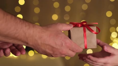Hands Exchange Christmas Present With Red Ribbon