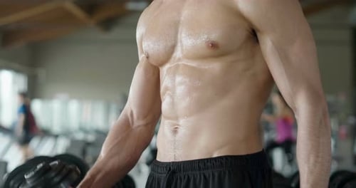 A shirtless guy at the gym, trains his body to stay fit and have defined muscles. The athlete rais