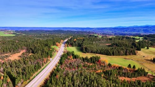Scenic view of a highway running through green fields and forests.