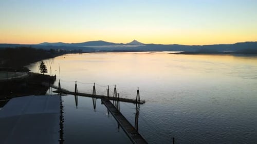 Drone flying above a stunning lake and dock, perfect scenery during a sunrise, surrounded by mountai