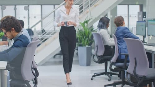 Une belle gérante apporte une tasse de café à son bureau et commence à travailler sur un ordinateur.