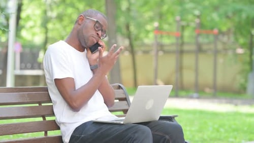 Man on Laptop Using Phone on Park Bench