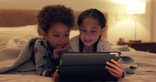 Children Lying on Bed Looking at Tablet