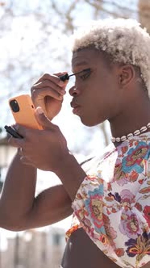 Focused Black Transgender Person Applying Mascara on Street