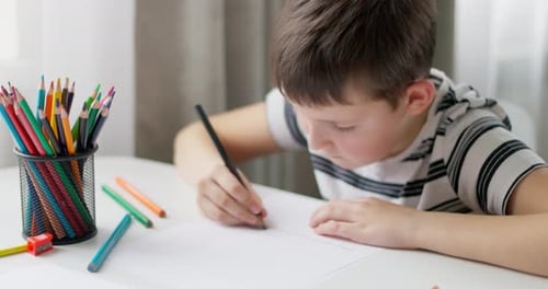 Child Drawing at White Table with Colored Pencils
