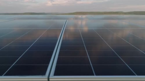 Solar panels reflecting the sky in a vast solar farm during sunset