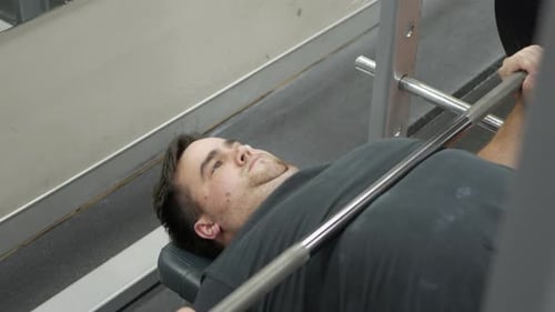 Young male performs a set of bench presses during a gym session.