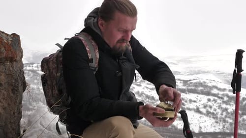 Hiker Opens Food on Snowy Mountain Top