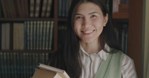 Portrait of Carefree Asian Girl Student Standing in University Library Holding Books Smiling Looking