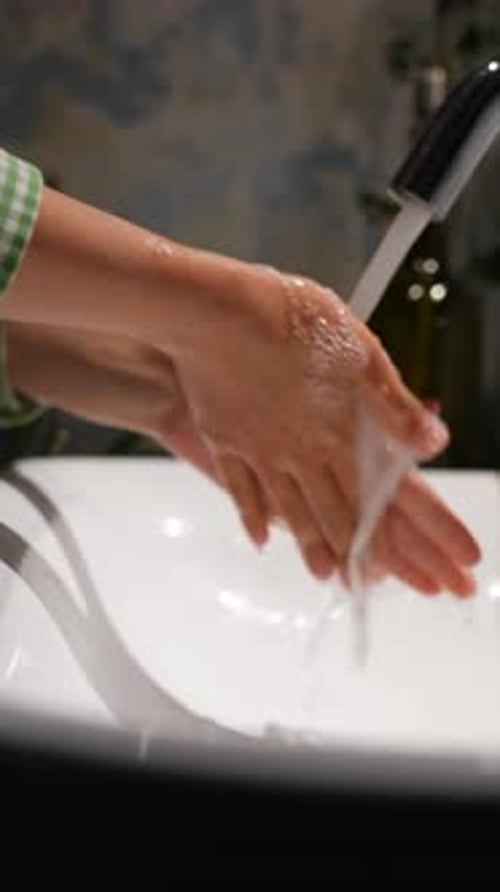Person Washing Hands at White Sink