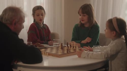 Grandfather and Three Young Girls Enjoy a Thoughtful Game of Chess Sharing Quality Family Time