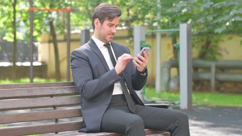 Suited Adult Using Phone on Park Bench
