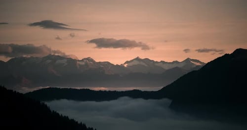 Misty Alpine Valley at Sunrise with Layered Mountain Peaks and Rolling Clouds