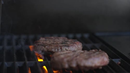 Slow Motion Close Up shot of two burger patties sizzling on a BBQ as orange flames shoot up from bel