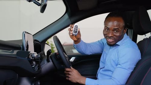 Portrait of a Happy Young Man Driving a New Luxury Car with Keys in a Car Dealership