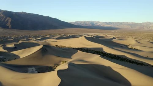 High, drone aerial shot of empty sand dunes in the desert, with mountains in background golden hour,