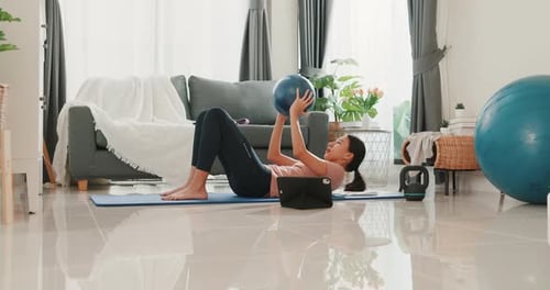 woman in sportswear watching fitness online video on tablet with fitness ball in living room.