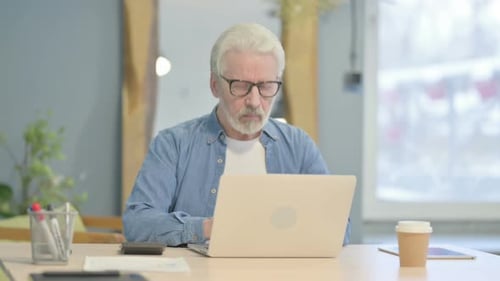 Man Typing on Laptop at Desk Looking at Camera