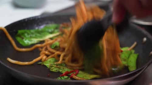 Preparing noodles on a pan in an Asian restaurant by a chef.