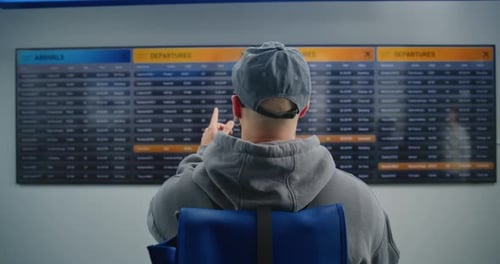 Airport Terminal Back View of Man with Backpack Checking His Flight on Digital Departure Board