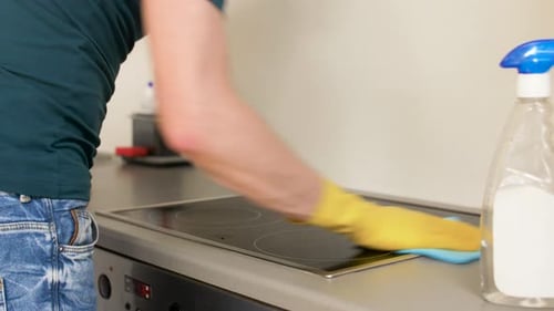 Man Cleaning Cooktop in Kitchen with Spray and Sponge