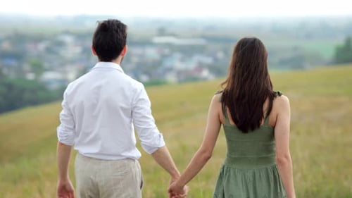 Couple Walks Holding Hands Across Field Against Blurred City