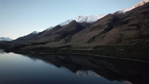 Aerial flying towards perfectly reflected snow capped mountains at sunset near Queenstown New Zealan