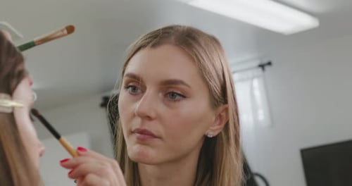 Woman applies makeup to another woman in a studio
