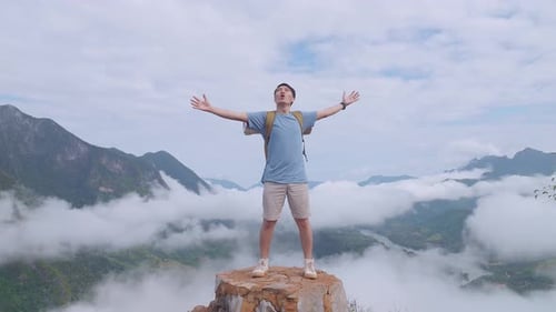 Hiker Male Standing On The Rock And Raising His Hands Celebrating Reaching Up Top Of Foggy Mountain