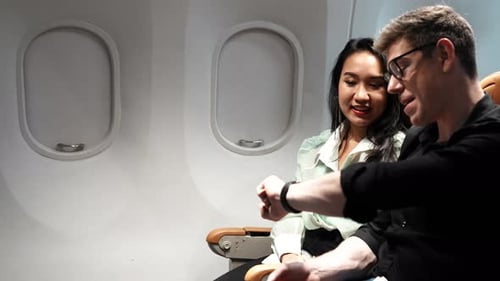 Couple on Airplane, Man Looking at Watch