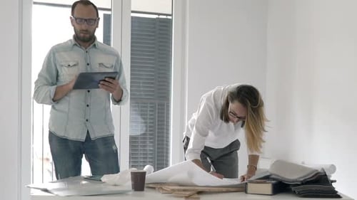 Two Architects with Tablet and Blueprints Working at Their New Apartment Analyzing