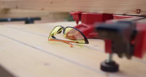 Hand Picks Up Safety Glasses On Wood Table