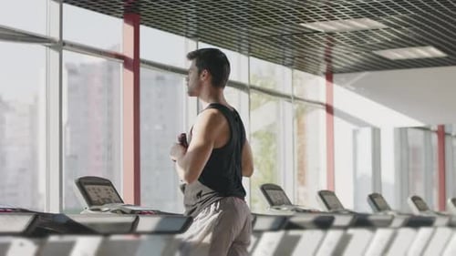 Man Runs on Treadmill Drinking Water in Gym