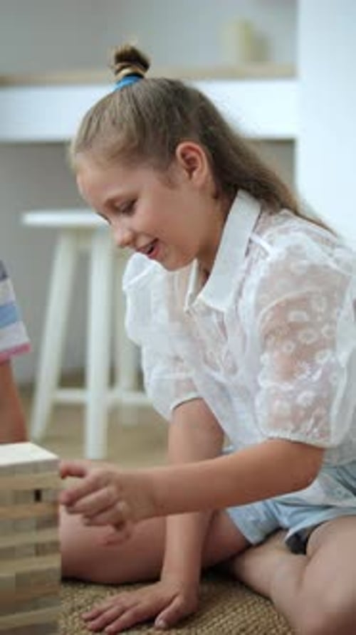 a Girl with Blonde Hair Pulls a Brick Out of a Wooden Jenga Tower