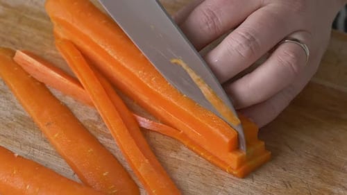 Slicing stack of carrots on a wooden cutting board in a close up shot
