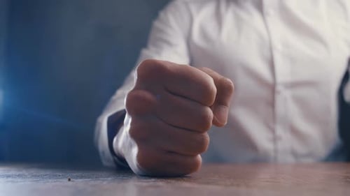 Man Clenches Fist on Table in Anger