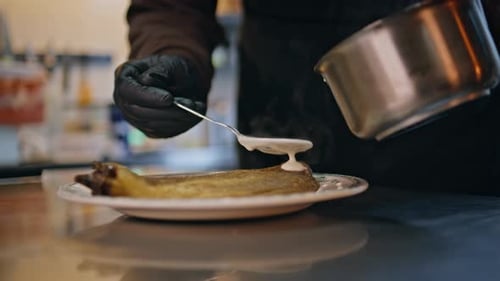 Chef Hands Pouring Sauce on Baked Eggplant in Restaurant Kitchen Closeup