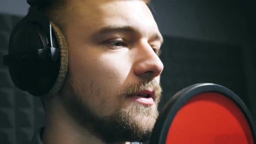 Male Singer in Headphones Singing Song Into the Microphone at Sound Studio