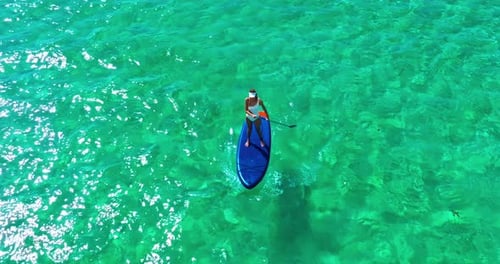 Aerial View of Woman in White Swimsuite Standing on Sup Board with Paddle on Crystal Turquoise Water