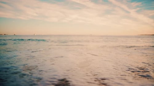 Nahaufnahme kleiner Meereswellen, die bei Sonnenuntergang sanft auf den Sandstrand rollen