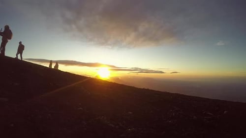 silhouetted hikers take photos to celebrate achievement of sunrise volcano hike