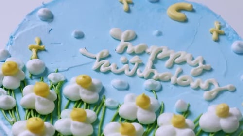 Close-up and zooming out of a birthday cake with blue frosting, decorated with small white flowers t
