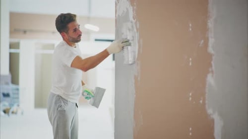 Young Adult Man Plastering Wall in Bright Room