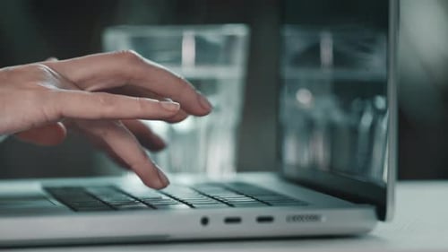 Fingers typing on laptop keyboard in office