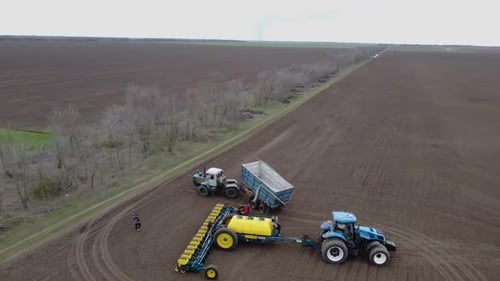 Blue tractor with yellow seeder working on the field in Ukraine OA