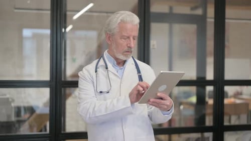 Senior Old Doctor Using Digital Tablet while Standing in Hospital