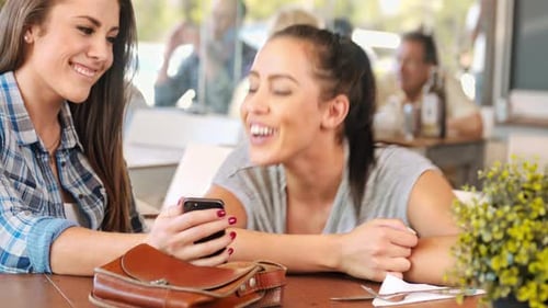 Two friends look at phone, laugh, and embrace